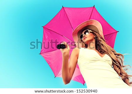 Beautiful young woman in elegant hat and sunglasses holding umbrella over sky.