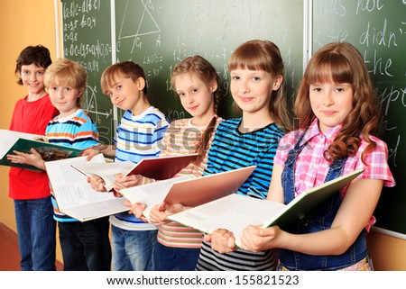 Group of happy schoolchildren standing with books at a classroom. Education.