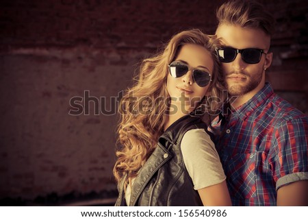 Couple Of Young People In Jeans Clothes Posing Outdoors Over Brick Wall.