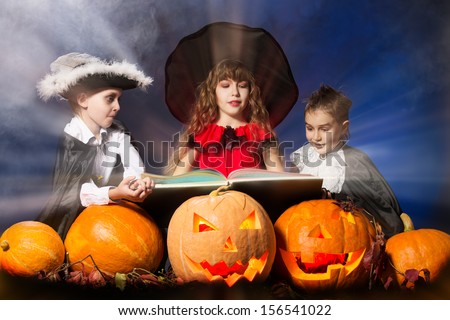 Cheerful children in halloween costumes standing with pumpkins and a book of spells. Over dark background.
