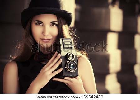 Beautiful Brunette Standing On A City Street And Holding The Old Camera. Retro Style.