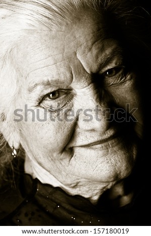 Black-and-white portrait of a happy senior woman smiling at the camera. Over black background.