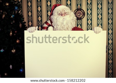 Santa Claus holding white board over home background.