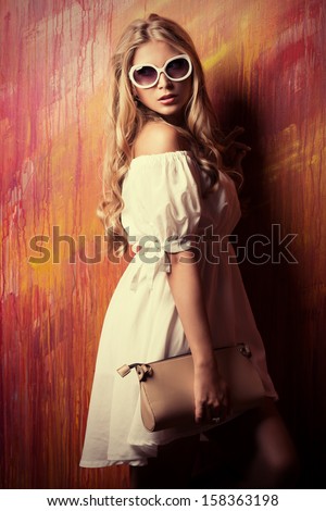 Charming Blonde Girl In Romantic White Dress And Sunglasses Over Vivid Background.
