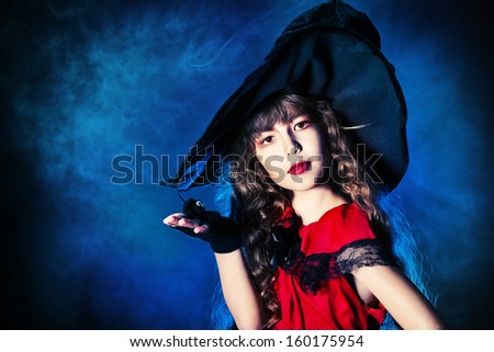 Pretty little girl in a costume of witch posing over dark background. Halloween.