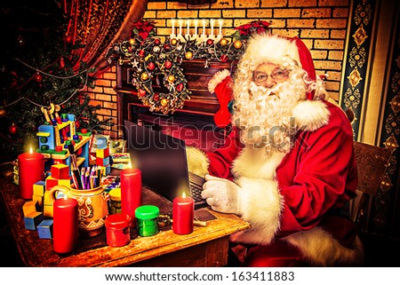 Modern Santa Claus sitting with a laptop at his home. Christmas.