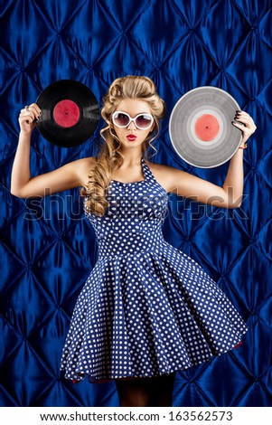 Pretty pin-up woman with retro hairstyle and make-up posing with vinyl record over vintage background.