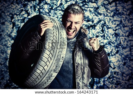 Handsome brutal man dressed in winter clothes covered with frost standing with car tire.