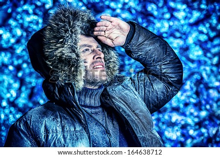 Handsome brutal man dressed in winter clothes covered with frost looking into the distance.