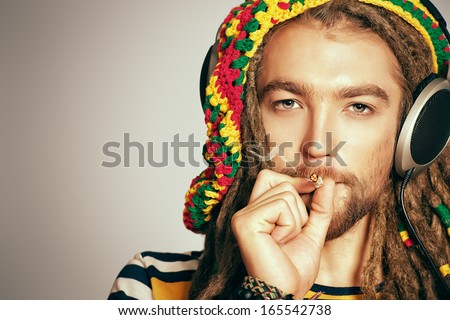 Portrait of a happy rastafarian young man listening to music in headphones.