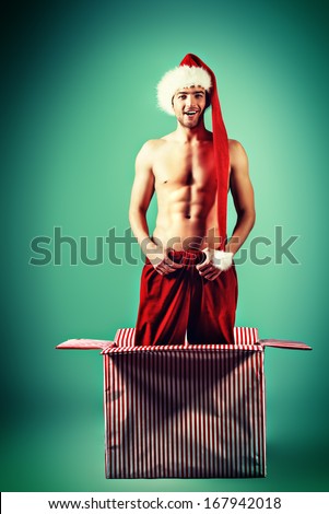 Sexual young man in Christmas hat posing with a huge present box.