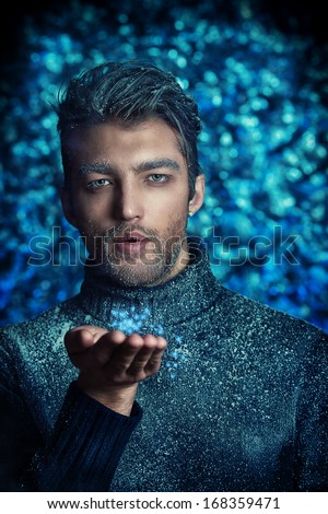 Portrait of a handsome man dressed in winter clothes, covered with frost blowing on snowflakes.