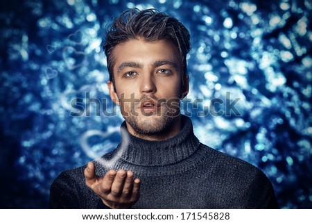 Portrait of a handsome man dressed in winter clothes, covered with frost blowing on snowflakes.