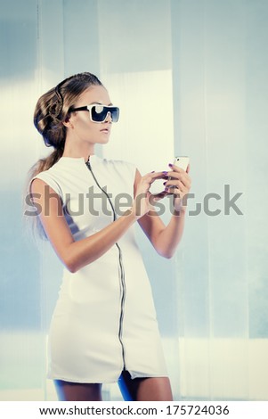 Futuristic young woman in white latex dress calling by cell phone. Sci-fi style.
