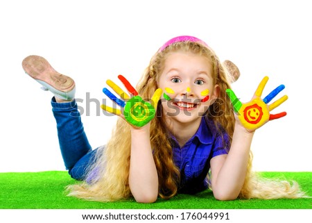 Laughing little girl painted in bright colors lying on green grass. Happy childhood.