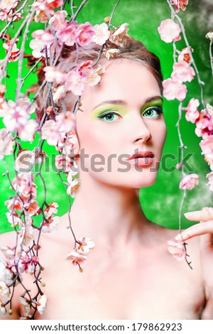 Portrait of a beautiful girl standing among the branches of cherry blossoms. Spring.