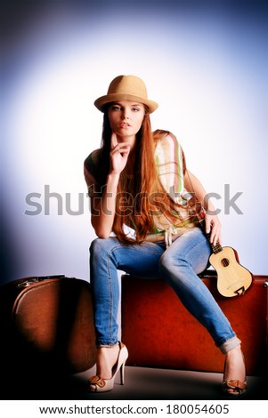 Attractive girl sitting on her old suitcases. Travel and tourism. Studio shot.
