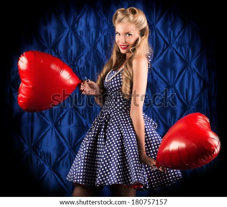 Charming pin-up woman with retro hairstyle and make-up holding red balloons in the shape of heart.