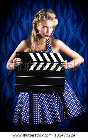 Pretty pin-up woman with retro hairstyle and make-up posing with clapper board over vintage background.