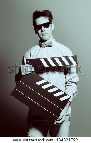 Extravagant young man holding clapper board. Cinema industry. Different occupations. Black-and-white photo.