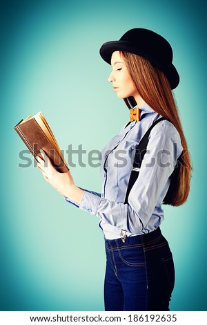 Elegant girl model in blouse, bow tie and bowler hat reading a book. Refined style of old Europe.