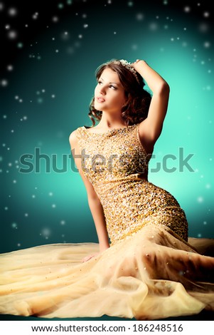 Fashion shot of a stunning woman in luxurious golden dress. Over dark background.