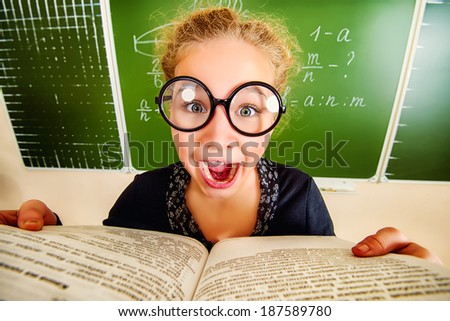 Funny schoolgirl in big round glasses opened the book and shouting at camera. Education.