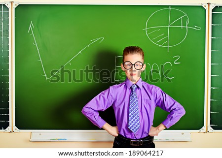 Smart schoolboy stands at the blackboard in the classroom with opened book. Education.