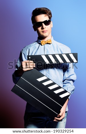 Extravagant young man holding clapper board. Cinema industry. Different occupations. Black-and-white photo.