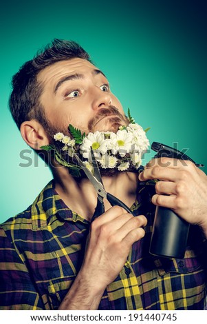 Funny and handsome young man cut his beard of flowers with scissors.