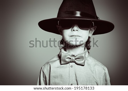 Portrait of a cute 7 year old boy wearing elegant hat and bow-tie with sunglasses.