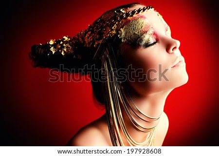 Art project: beautiful woman with golden make-up. Jewelry, make-up. Fashion. Over red background.
