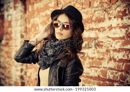 Beautiful young woman in black leather jacket posing over brick wall.