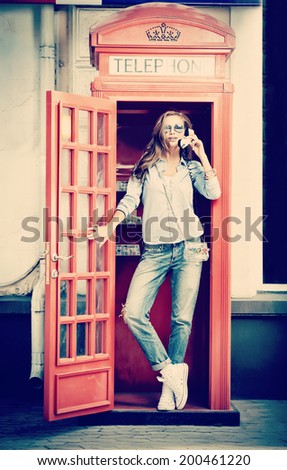 Pretty young woman talking on the phone in telephone booth. Europe, England. Vacation, tourist trip.