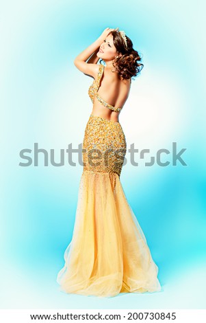 Fashion shot of a stunning woman in luxurious golden dress. Full length portrait.