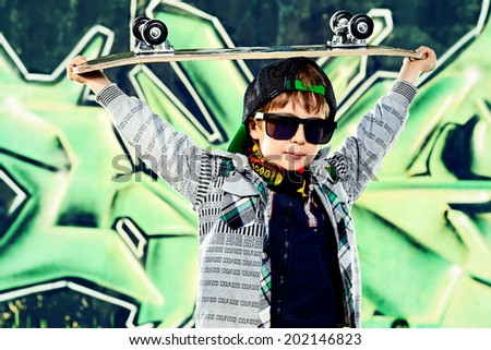 Cool 7 year old boy with his skateboard on the street. Graffiti background. Childhood. Summertime.