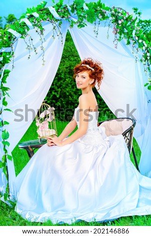 Beautiful bride with chaming red hair sitting under the wedding arch. Wedding dress and accessories. Wedding decoration.