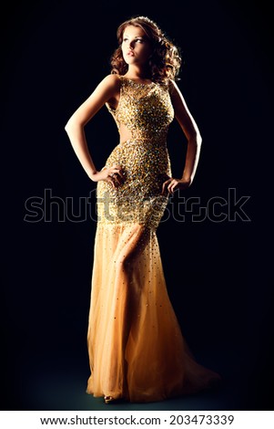 Fashion shot of a stunning woman in luxurious golden dress. Over black background.