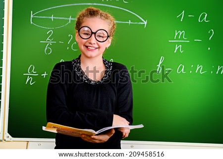 Funny schoolgirl in big round glasses opened the book and looking at the camera. Education.