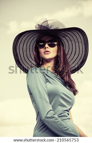 Portrait of a charming lady in beautiful elegant dress and hat against the sky.