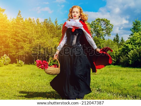 Beautiful blonde woman in  old-fashioned dress and red cloak walking in the meadow with a basket of tulips.