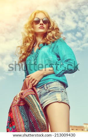 Gorgeous young woman with beautiful wavy hair wearing casual blouse and jeans shorts posing outdoor. Fashion shot.