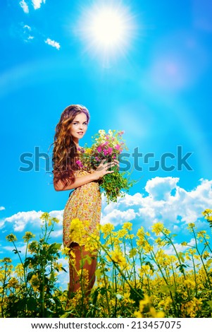 Happy young woman standing in a field of blooming yellow flowers. Summer.