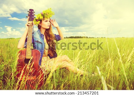 Romantic girl in a wreath of wild flowers playing her guitar. Summer. Hippie style.