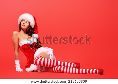 Full length portrait of an attractive young woman in Santa Claus costume over red background. Christmas.