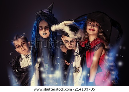Cheerful children in halloween costumes posing over dark background.