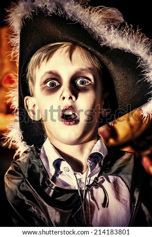 Little boy in halloween costume of pirate posing with pumpkins over dark background .