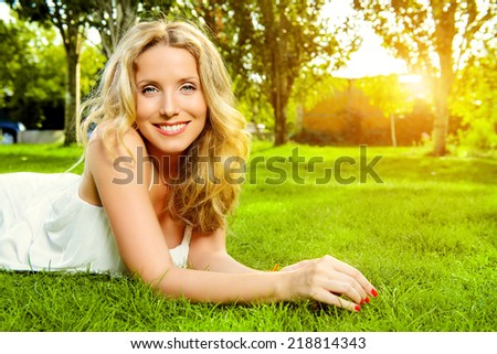 Close-up portrait of a beautiful smiling woman lying on a grass outdoor. She is absolutely happy.