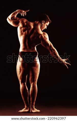 Beautiful muscular man bodybuilder posing back over dark background. Full length.