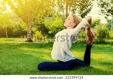Beautiful young woman doing yoga stretching exercise in the summer park. Healthy lifestyle. Yoga.